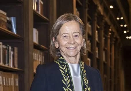 Portrait de Dominique Senequier, souriante, en habit vert brodé d'académicienne, devant des rayonnages de bibliothèque.